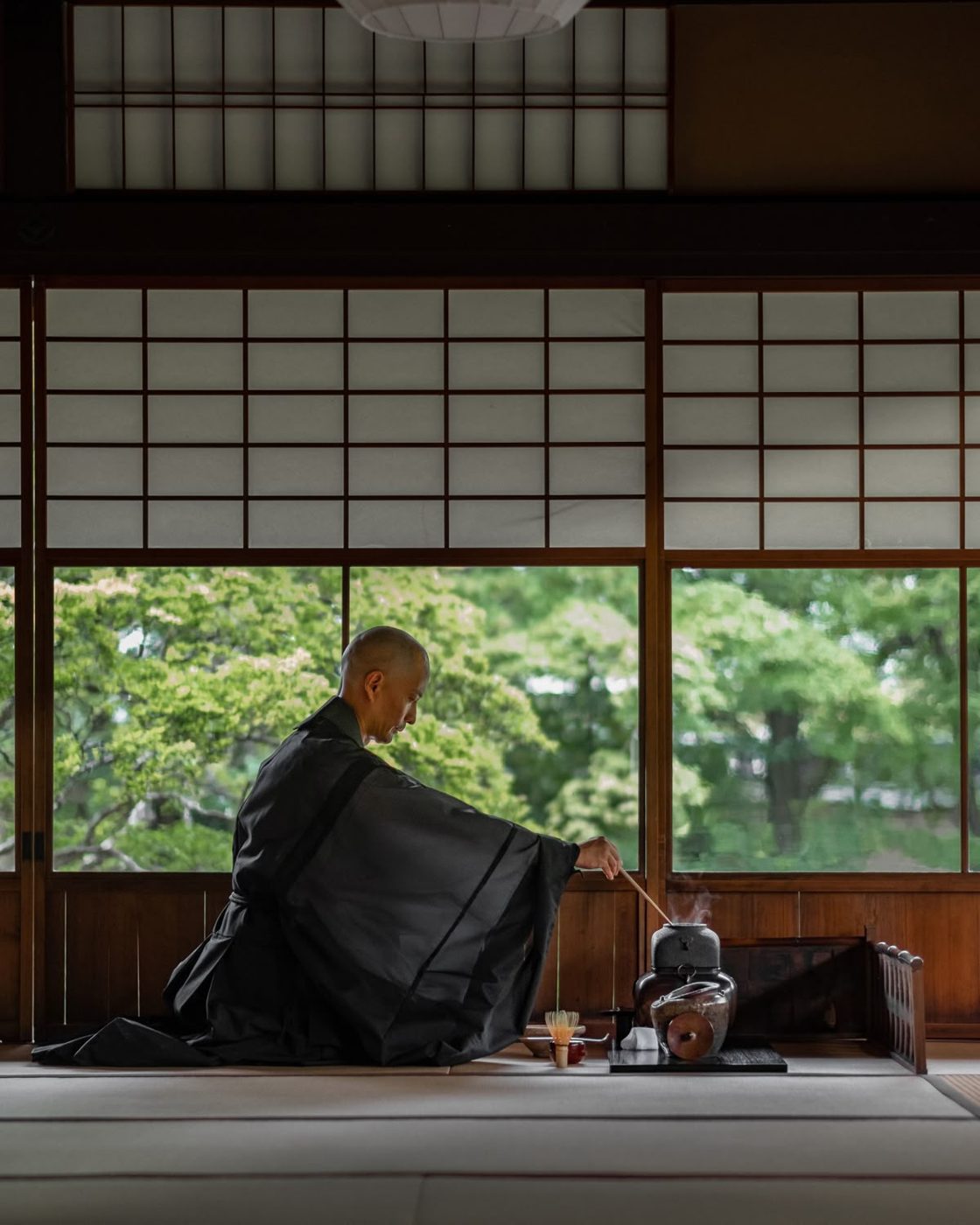 A monk preparing tea in a tatami room overlooking a garden